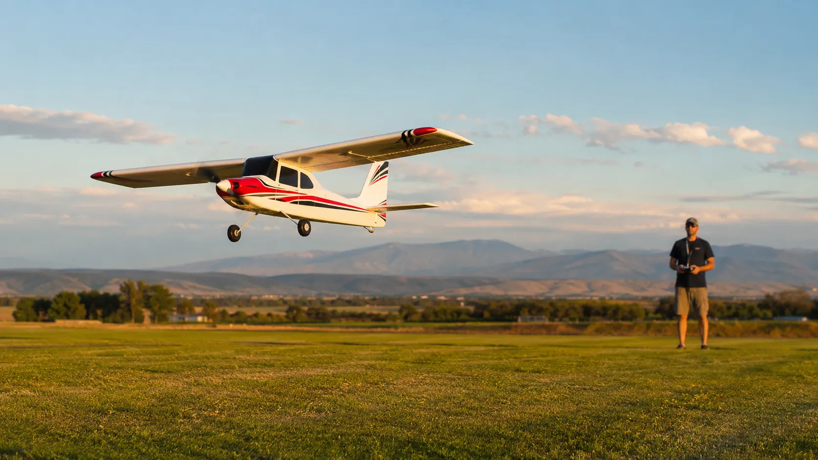Small RC airplane flying over a grassy field with a person holding a remote control.