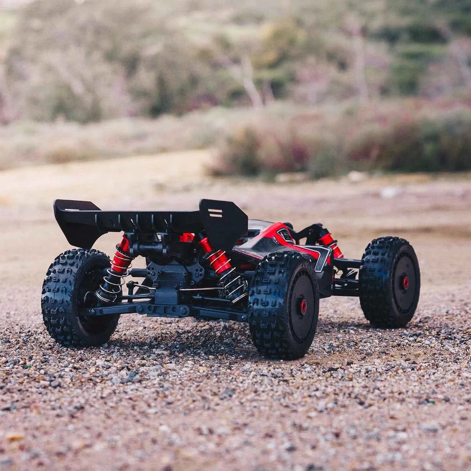 Black and red off-road RC buggy on a gravel surface with a blurred natural background