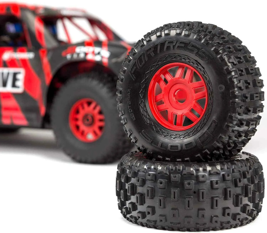 Close-up of two black off-road tires with red centers, blurred red and black vehicle in the background.