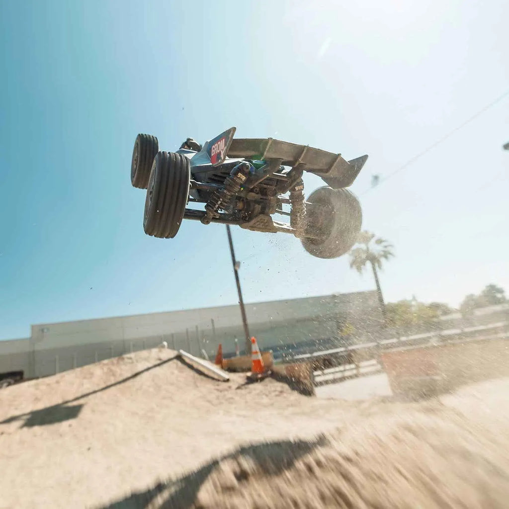 Off-road rc buggy performing a jump on a dirt track with a clear blue sky.