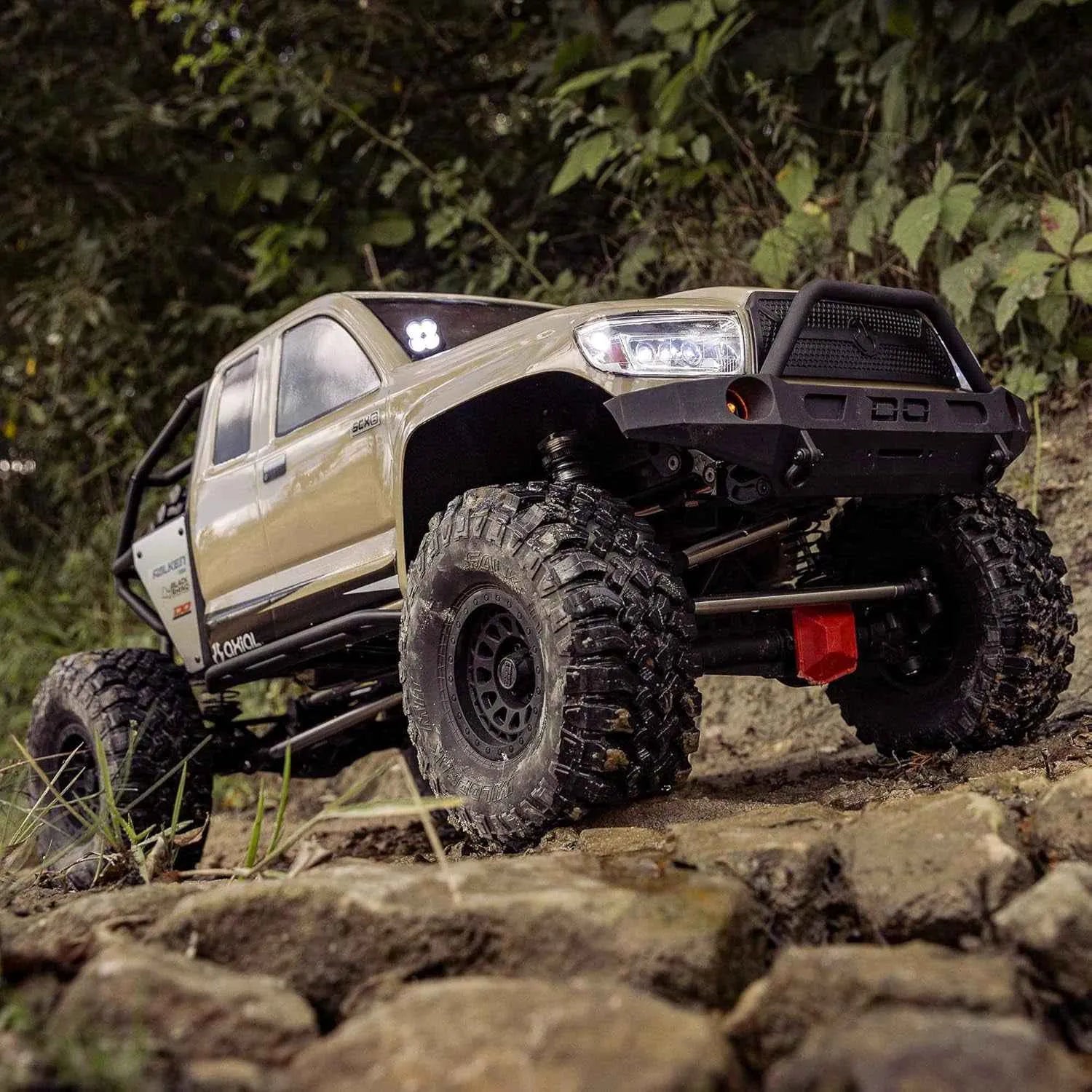 Off-road RC crawler climbing a rocky terrain with greenery in the background
