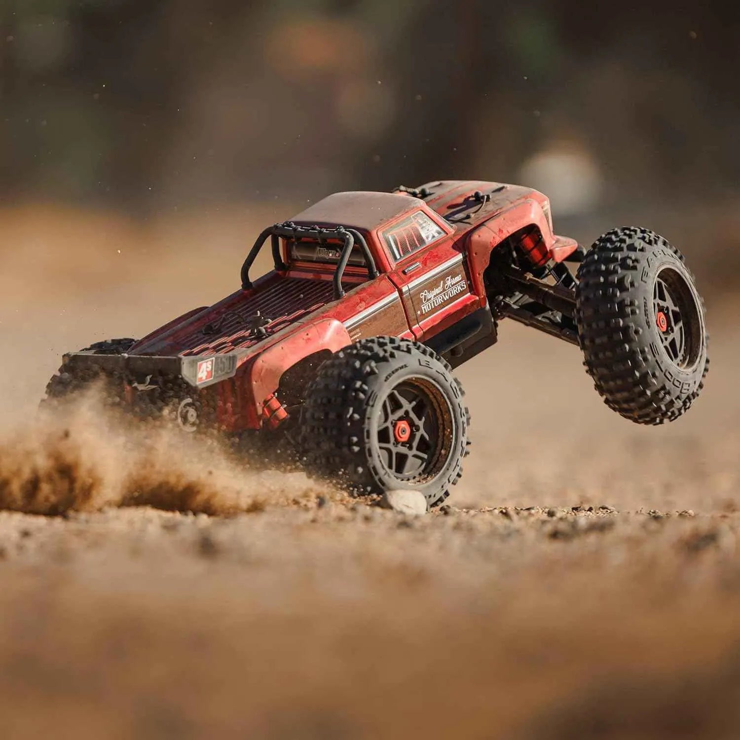 Red off-road rc stunt truck driving on a dirt surface with a blurred background