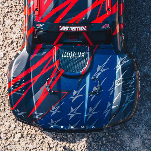 Top view of a red and blue Arrma Mojave RC short course truck on a gravel surface.