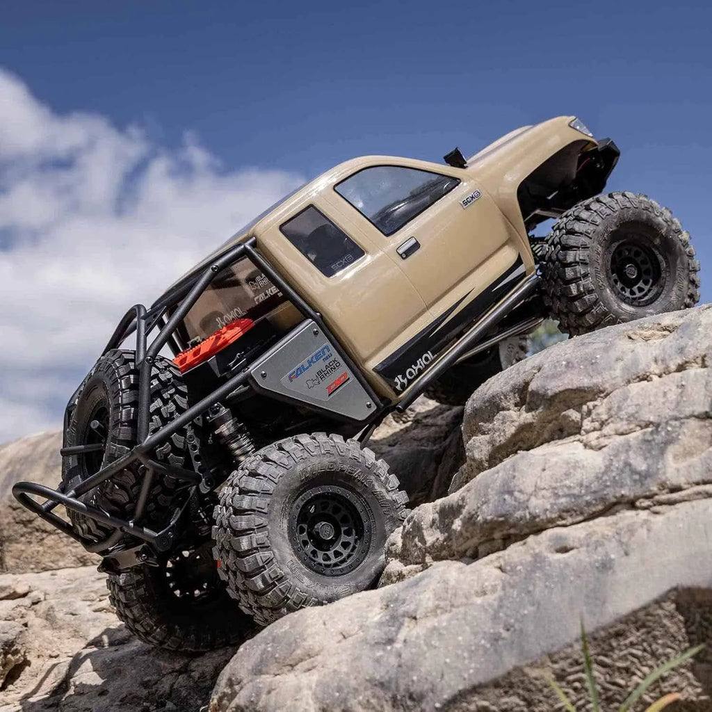 Beige off-road crawler climbing rocky terrain with a clear blue sky.