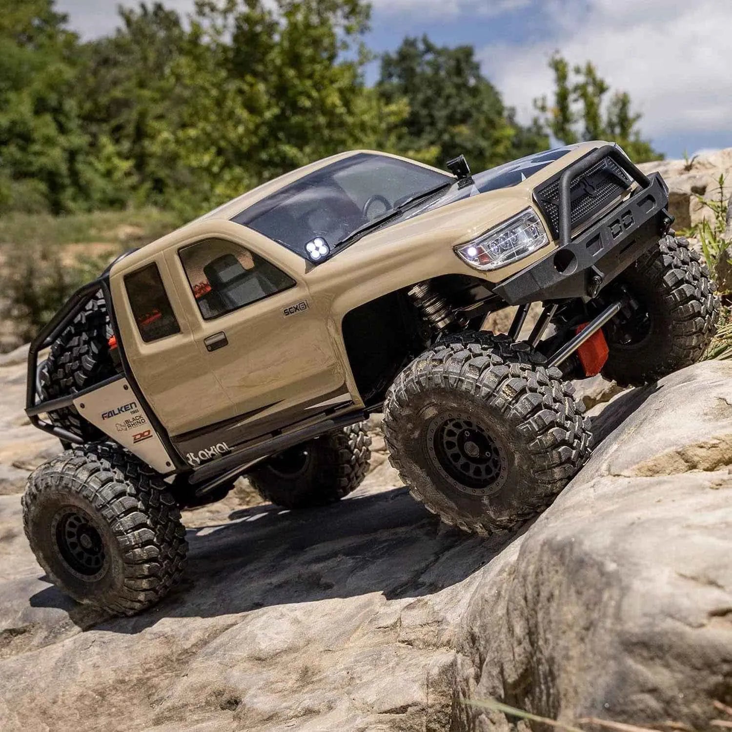 Beige off-road RC crawler climbing a rocky hill with greenery in the background