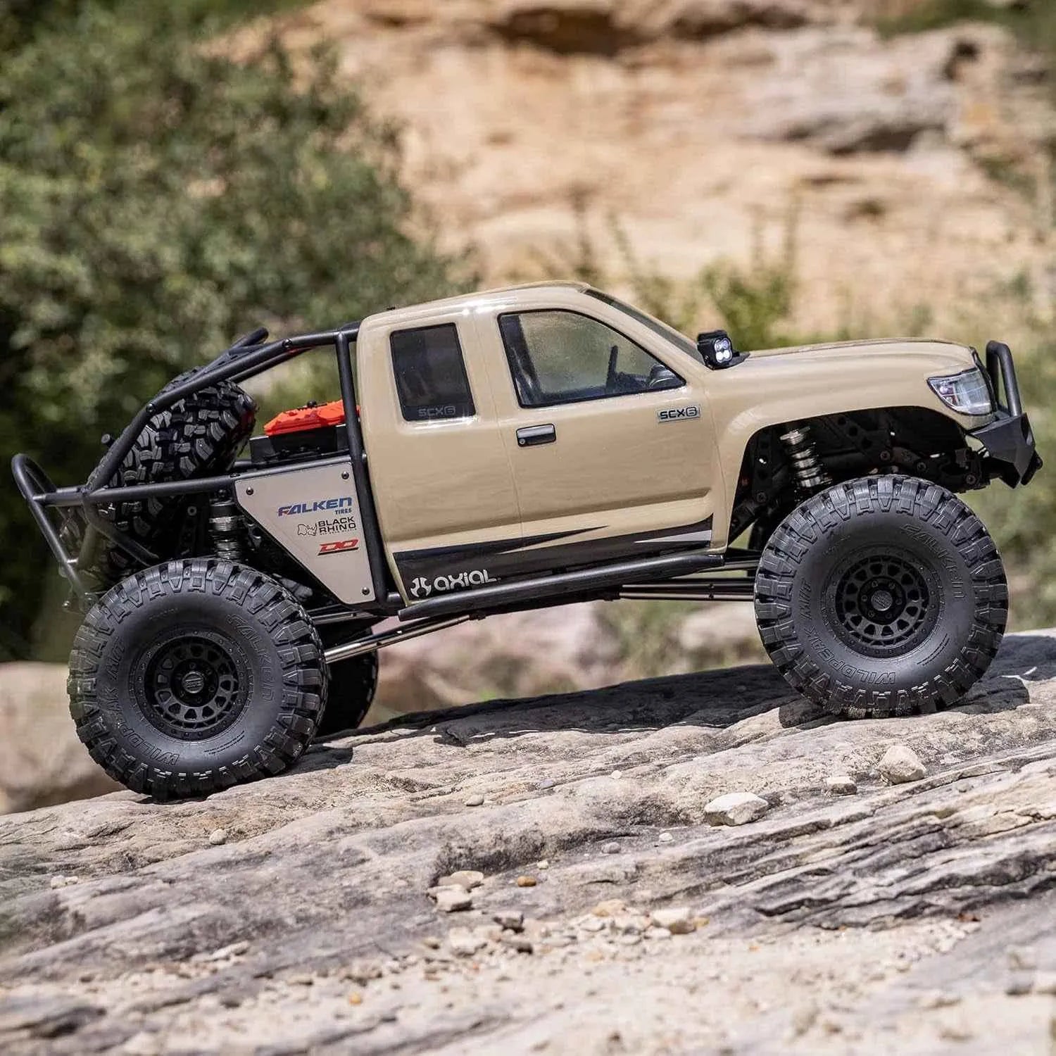 Beige off-road RC crawler on a rocky surface with a natural landscape background