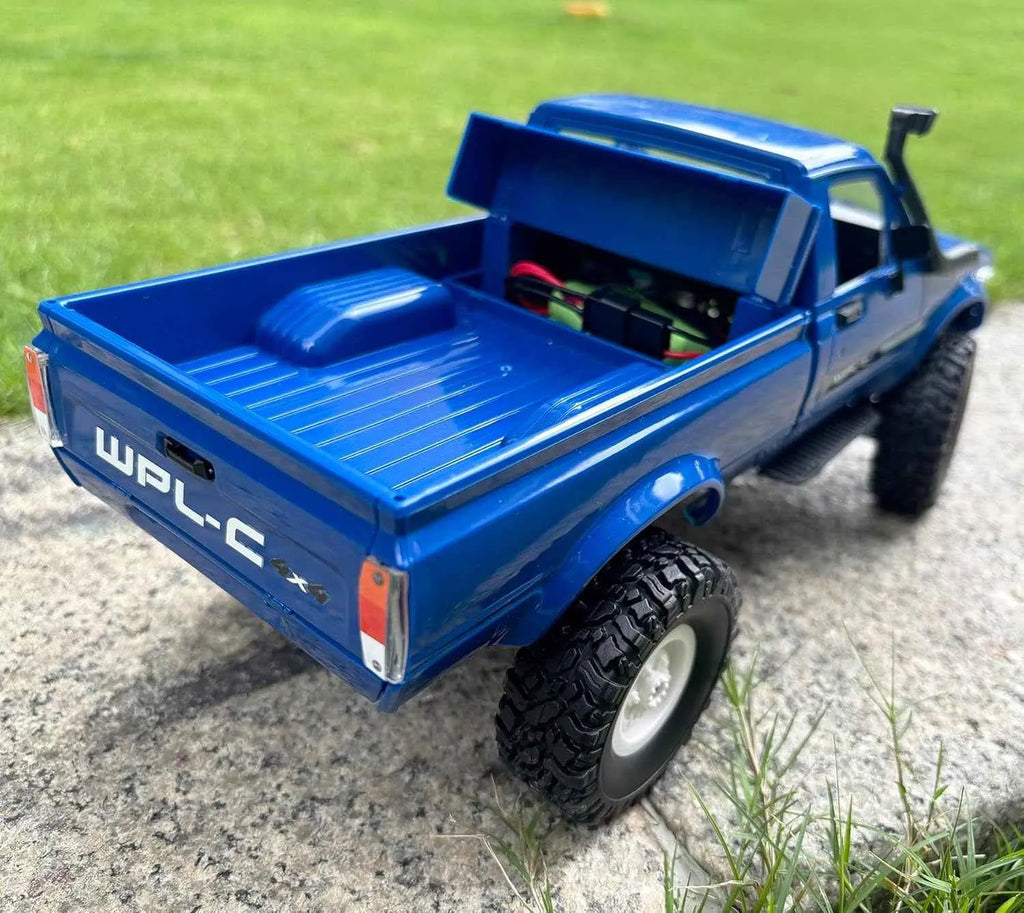 Blue RC crawler with open bed on a concrete surface and grass background
