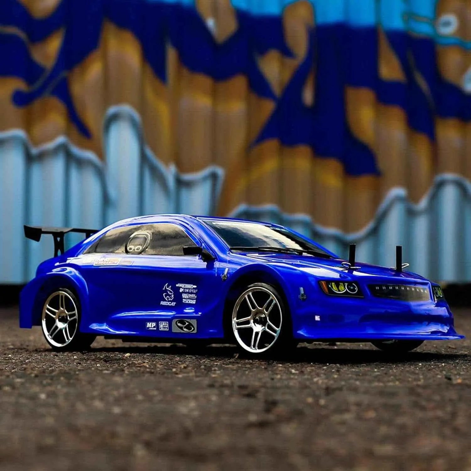 Blue rc drift car on a dirt surface with a colorful mural in the background