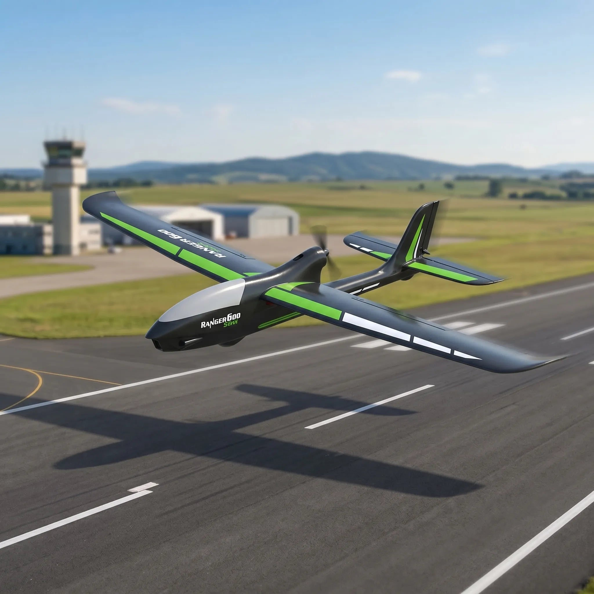 Green and gray RC plane on a runway with airport and mountains in the background