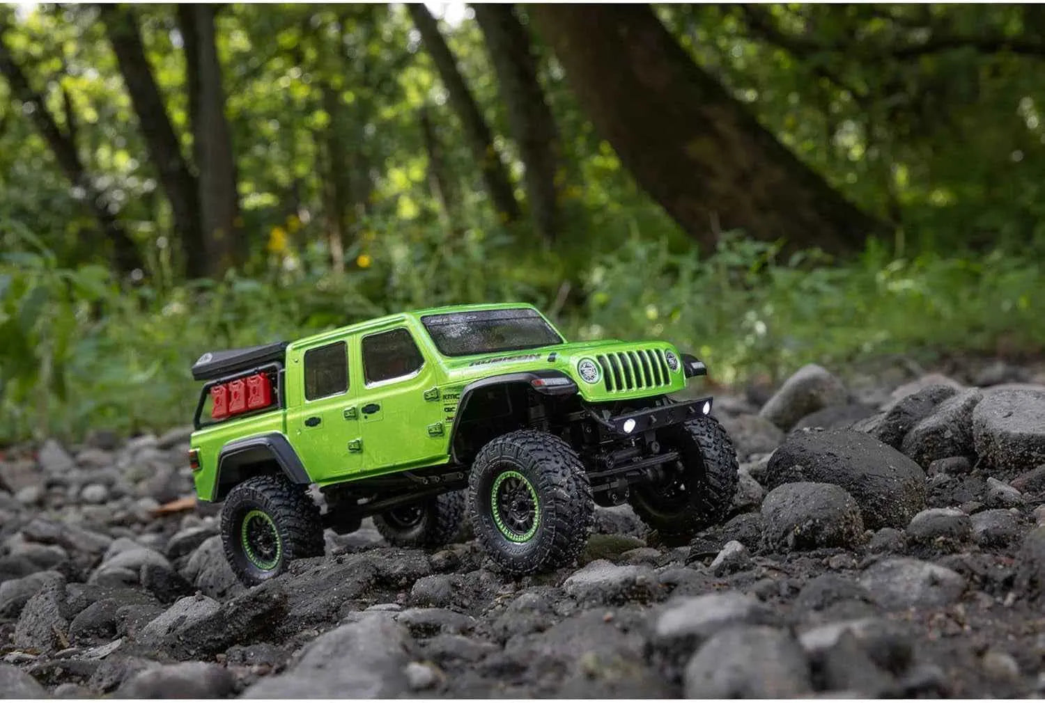 Green RC crawler on rocky terrain with a forest background