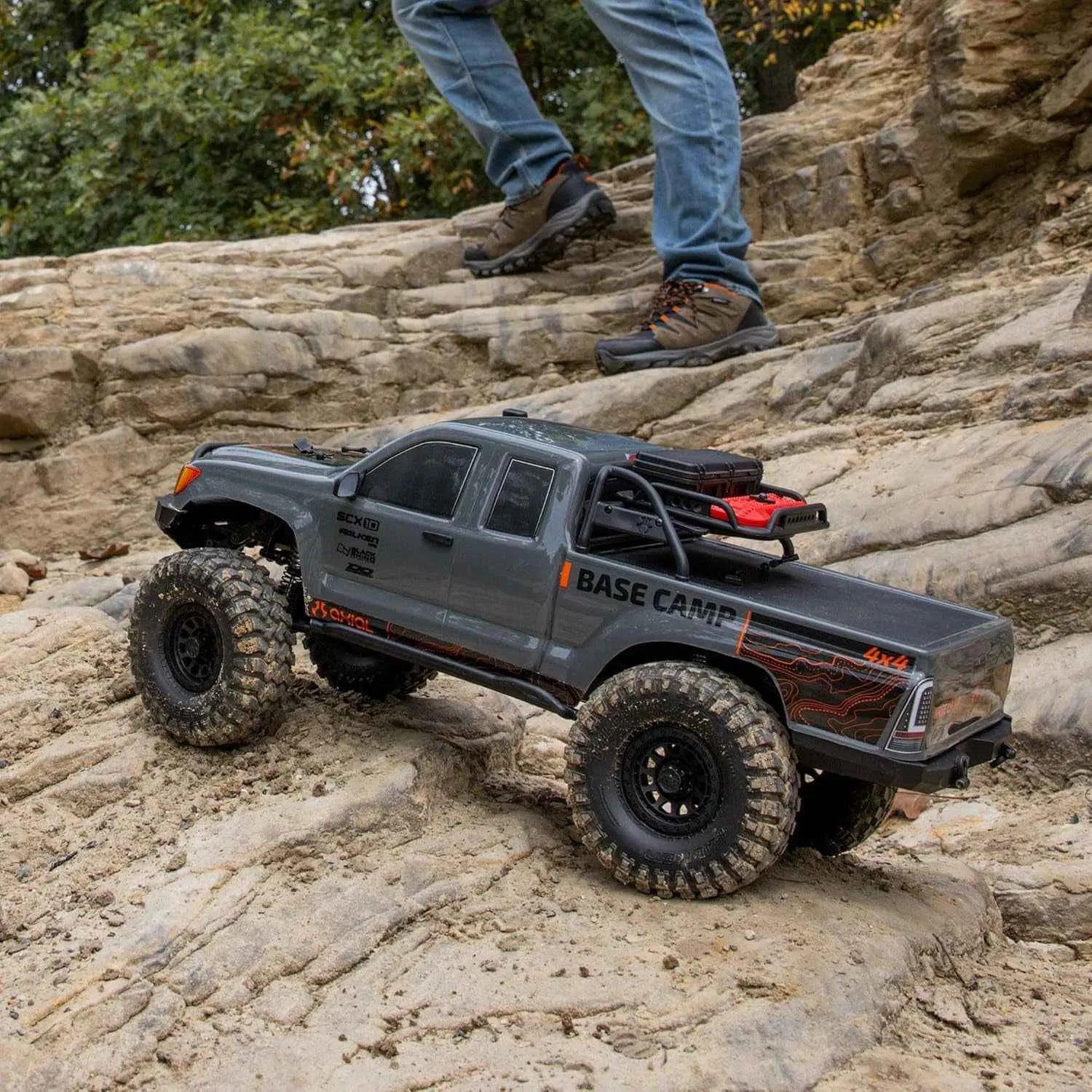 Model RC crawler on rocky terrain with person in background