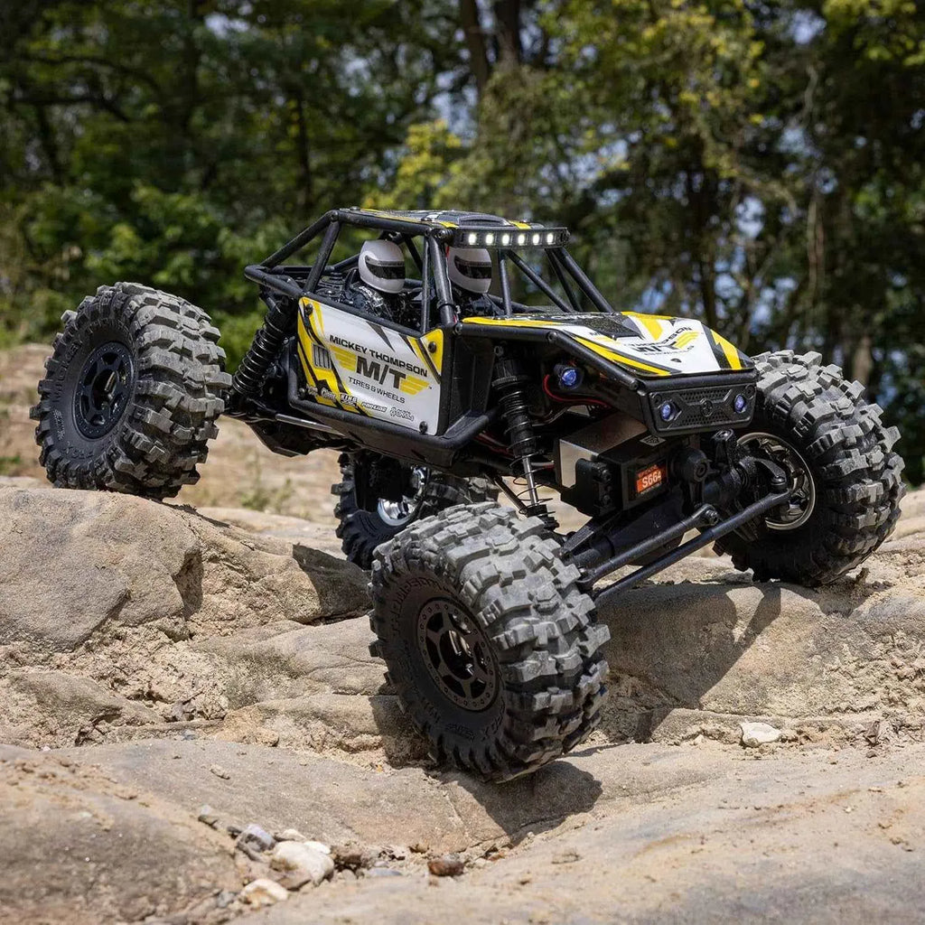 Off-road RC crawler climbing a rocky terrain with trees in the background