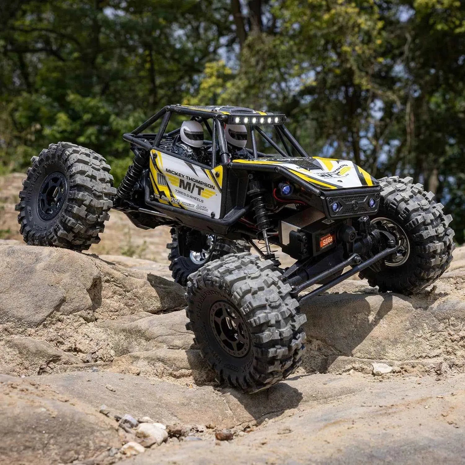 Off-road RC crawler climbing a rocky terrain with trees in the background