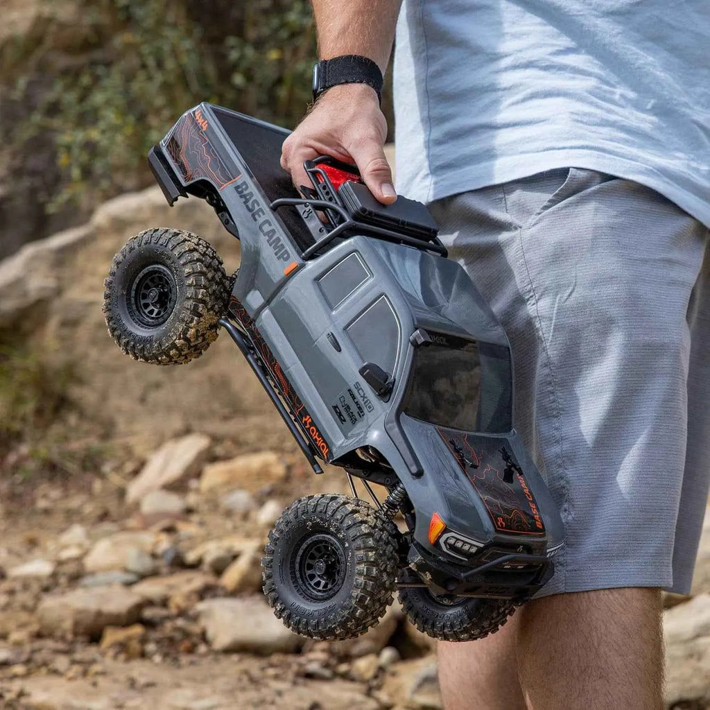 Person holding a remote-controlled off-road crawler in an outdoor setting