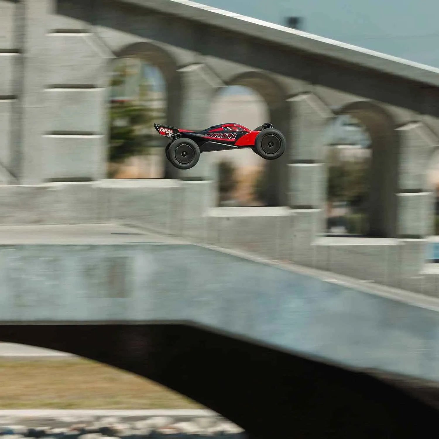 Red and black RC buggy in mid-air over a concrete ledge with a blurred background
