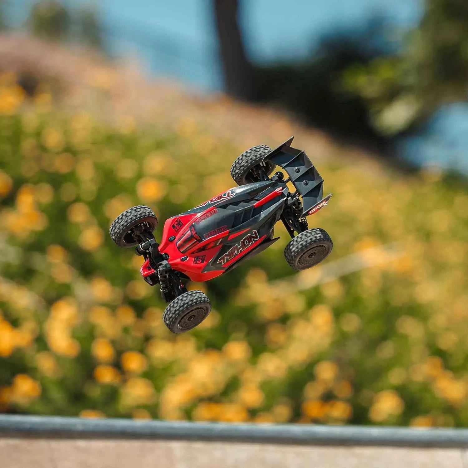 Red and black remote control buggy in mid-air with a blurred natural background
