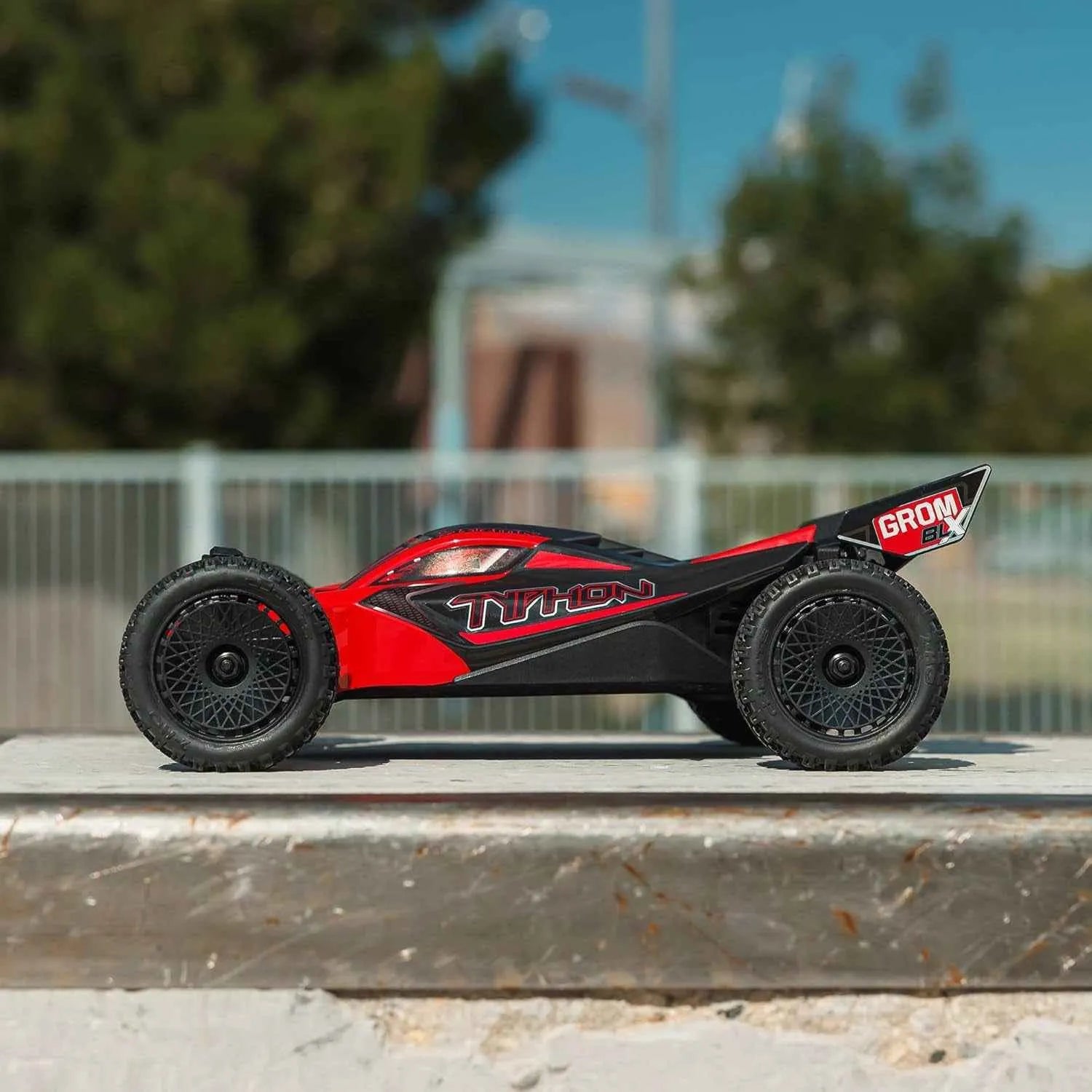 Red and black remote control buggy on a concrete surface with blurred background