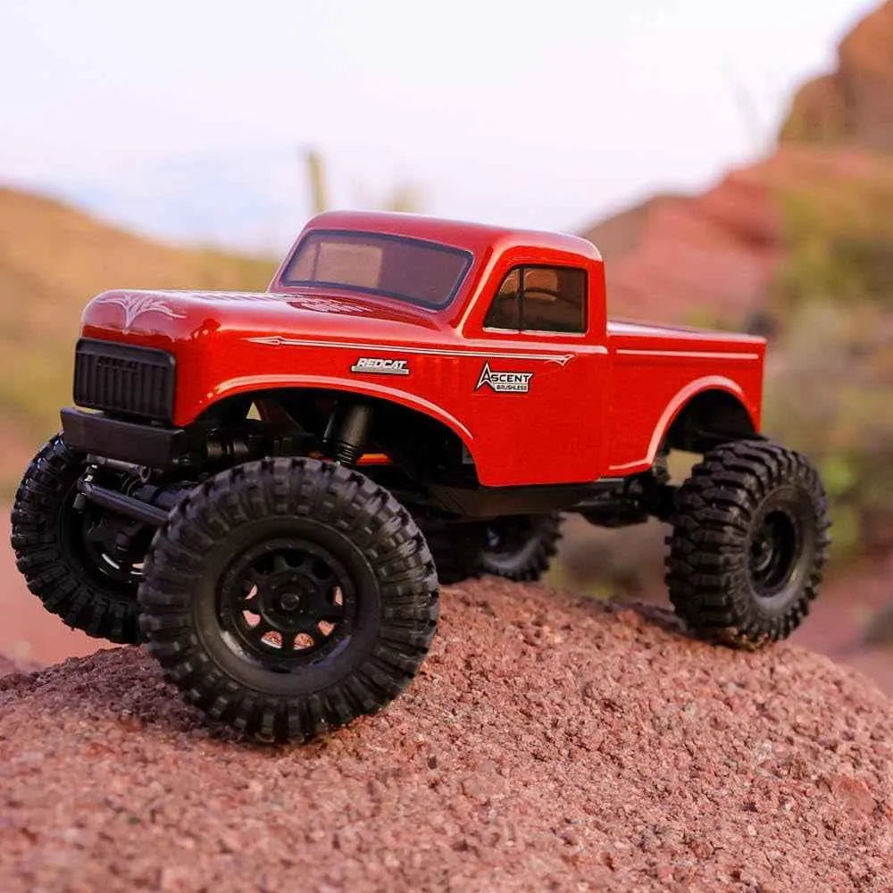Red RC rock crawler with large black wheels on a rocky surface