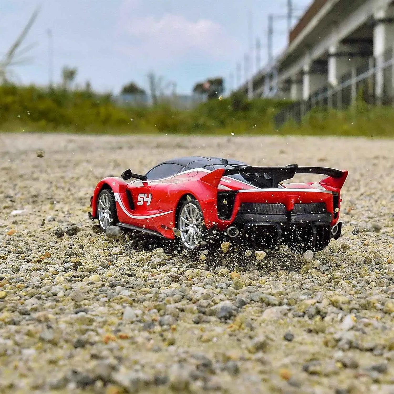 Red sports car with number 54 driving on a gravel surface.