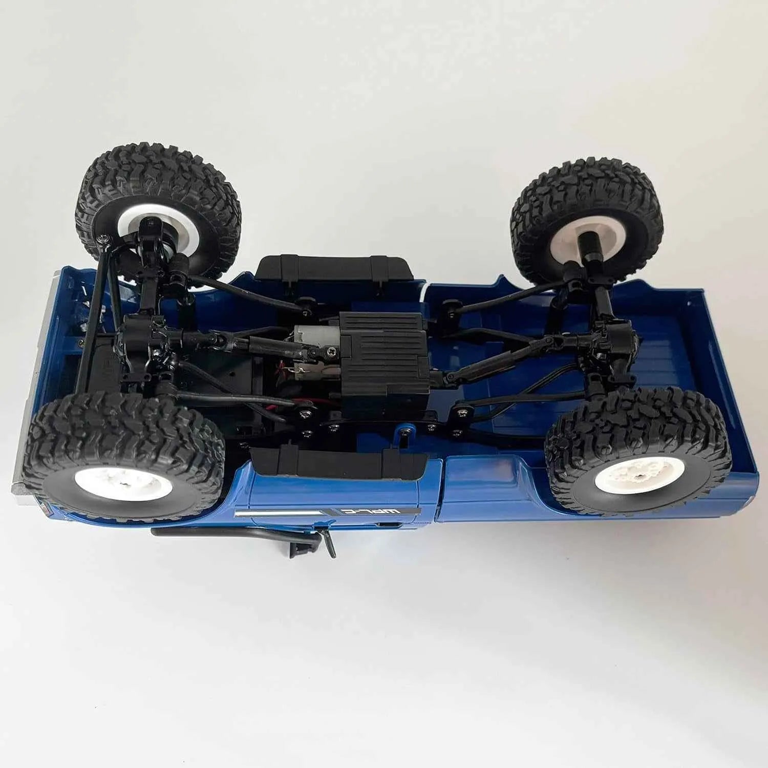 Top view of a blue RC crawler chassis with large black tires on a white background